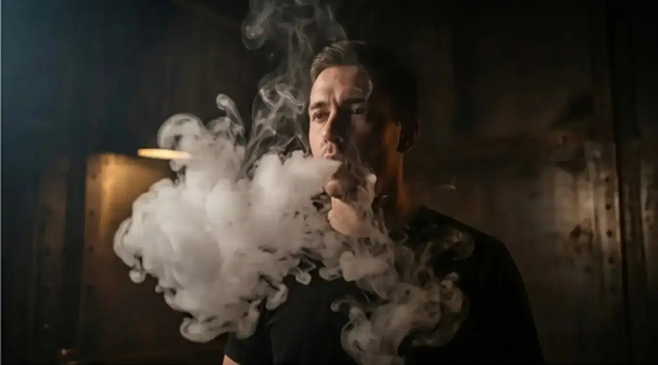 Unnamed vape device held in hand producing large white vapor clouds against dark background